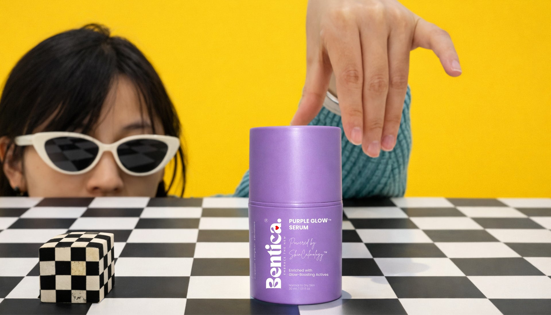 Person holding a purple container labeled 'Bentica' on a checkered table with a yellow background